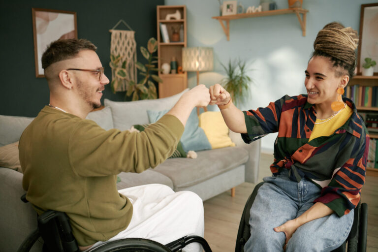 Smiling Man and Woman in Wheelchairs Giving Fist Bump Celebrating Event at Home